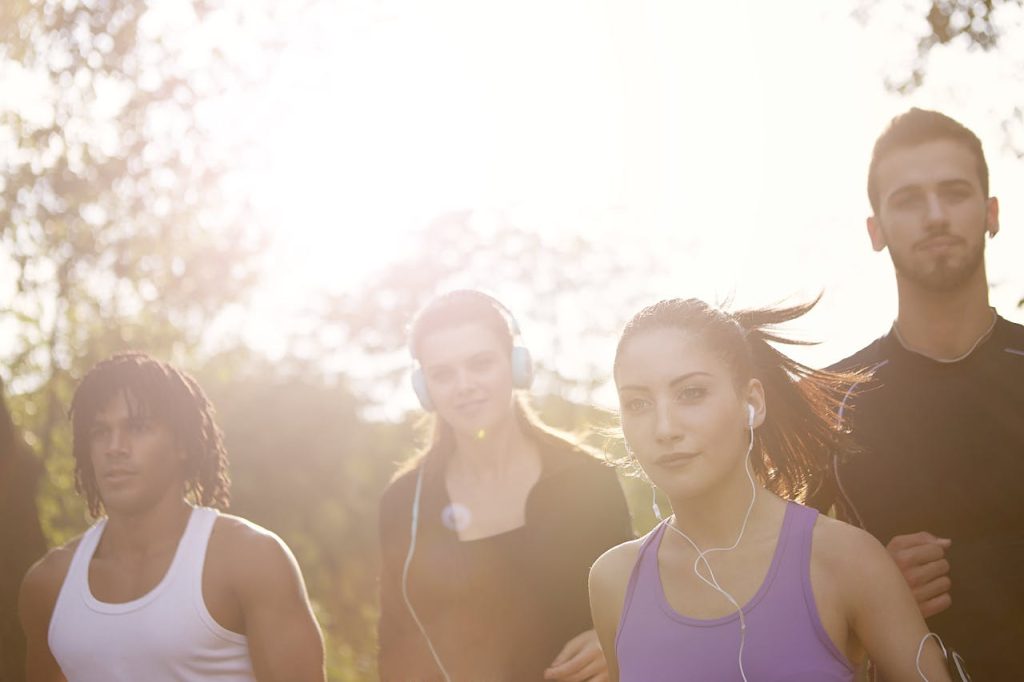 Group of young multiracial women with earphones and men in sportswear running together on sunny day in park